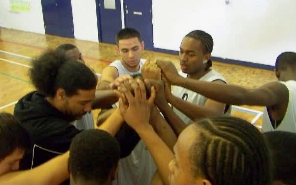 Coach Leon and basketball teammates joining hands in a team huddle